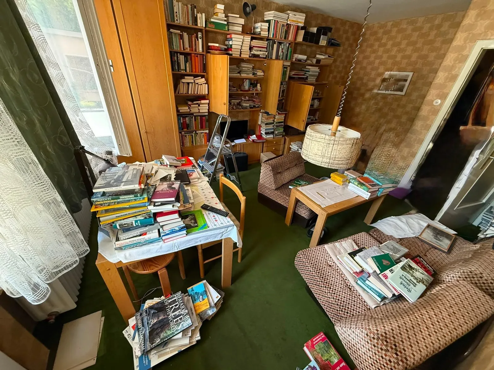 Wohnzimmer mit Bücherstapeln, Sessel und Tisch vor der Entrümpelung in Duisburg